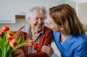 A caregiver checks in a on happy senior caring for a plant in their assisted living community apartment.
