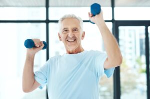 A smiling older adult with raised arms and dumbbells in both hands.