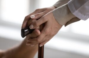 Close-up of a caregiver's hands gently supporting another person's hand resting on a cane.