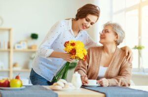 An adult child brings their senior parent a colorful bunch of flowers and stays for a short, calm visit to prevent overstimulation.