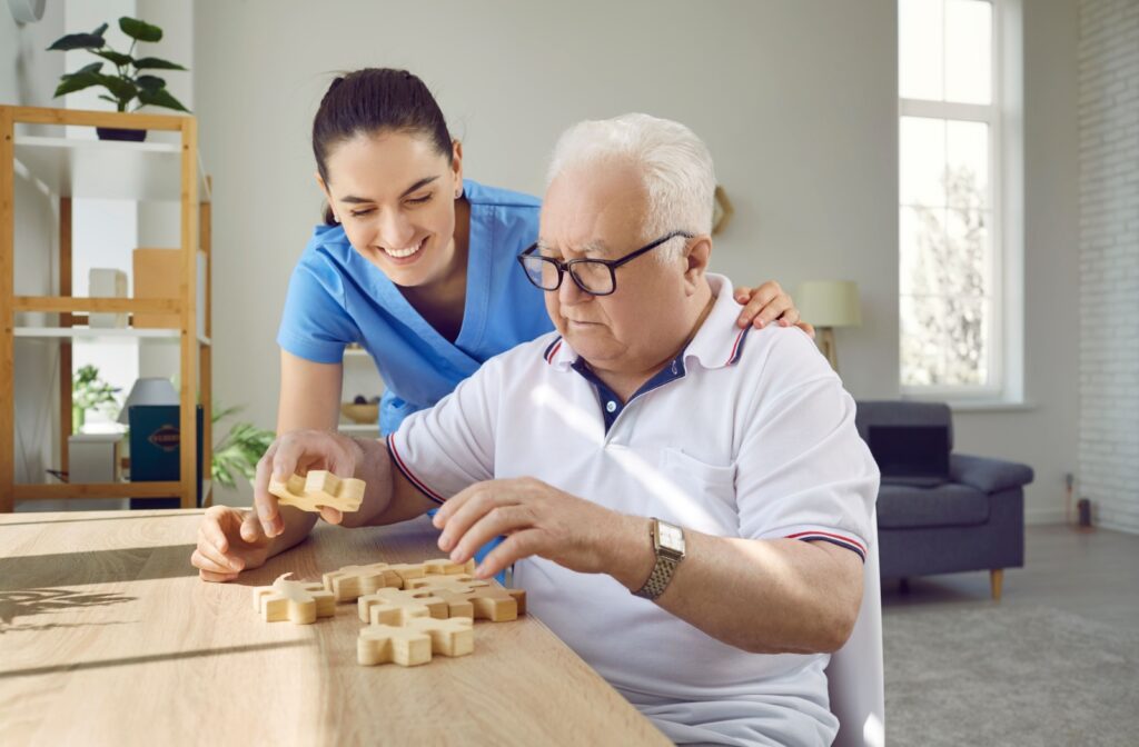 Older man engaging in a puzzle activity with assistance from a caregiver.