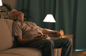  A senior who has fallen asleep on the couch during the day while watching TV, a remote in their hand