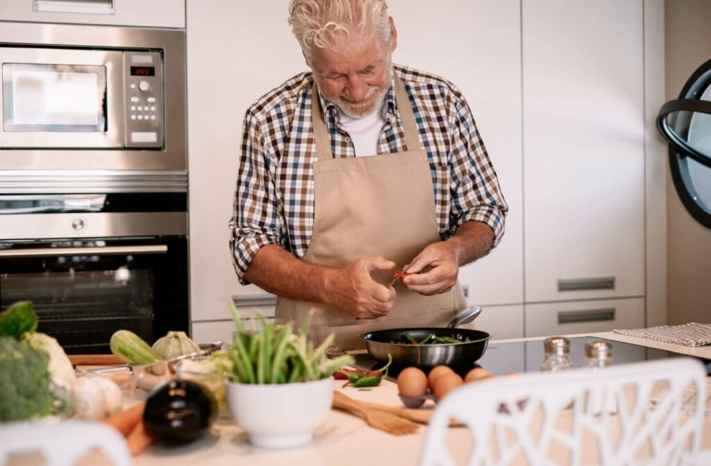 An older man wearing an apron and preparing a meal in a kitchen.