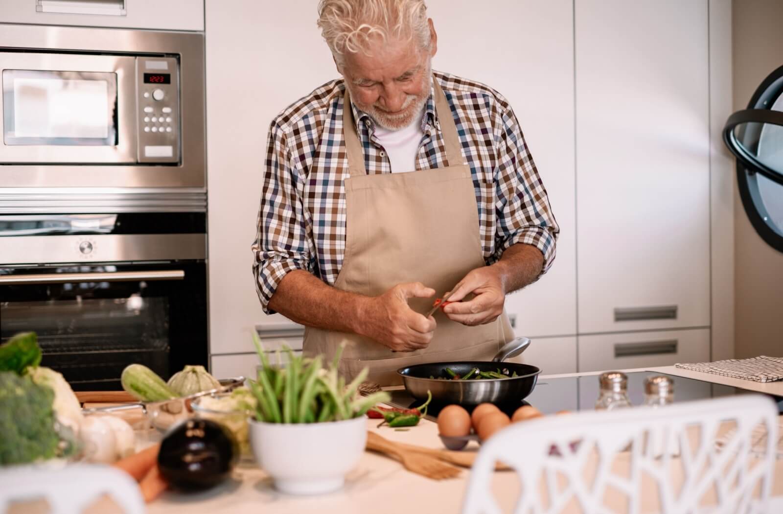 An older man wearing an apron and preparing a meal in a kitchen.