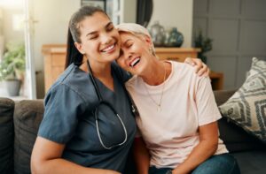 An older adult in assisted living laughing and resting their head on the shoulder of their on-site nurse