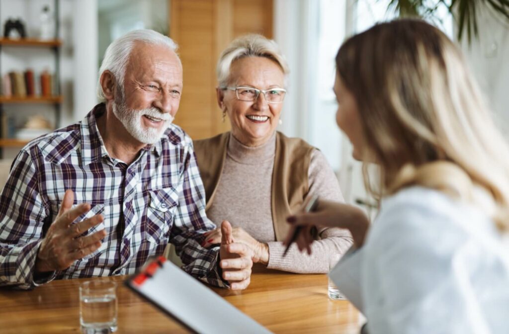 An older couple in assisted living smiling and sitting across the desk from their on-site nurse during a regular checkup