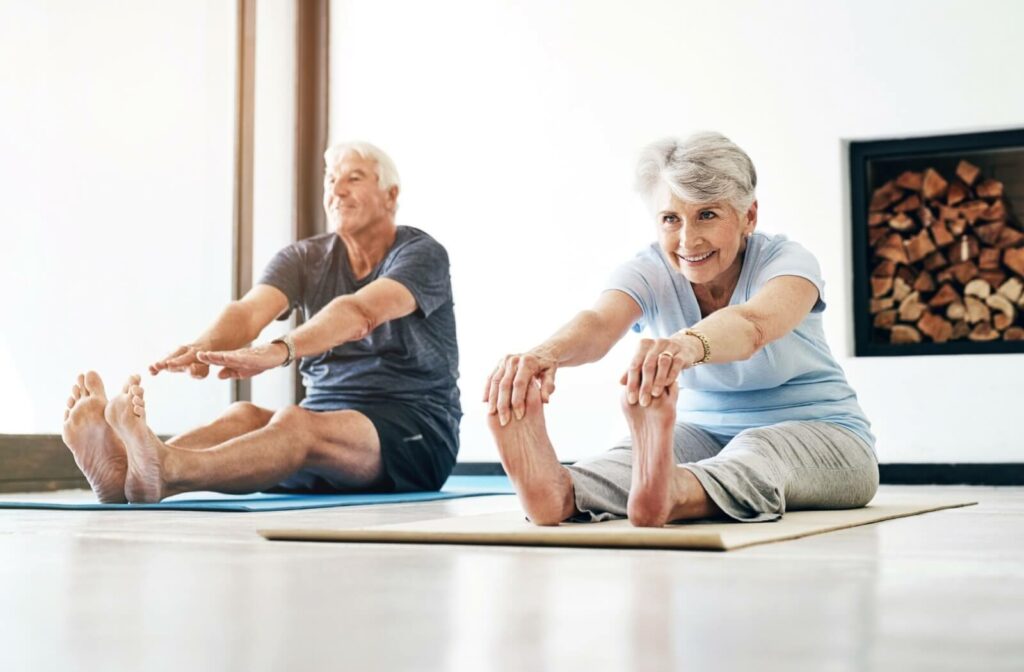 An older couple on yoga mats stretching forward during an exercise routine in senior living.