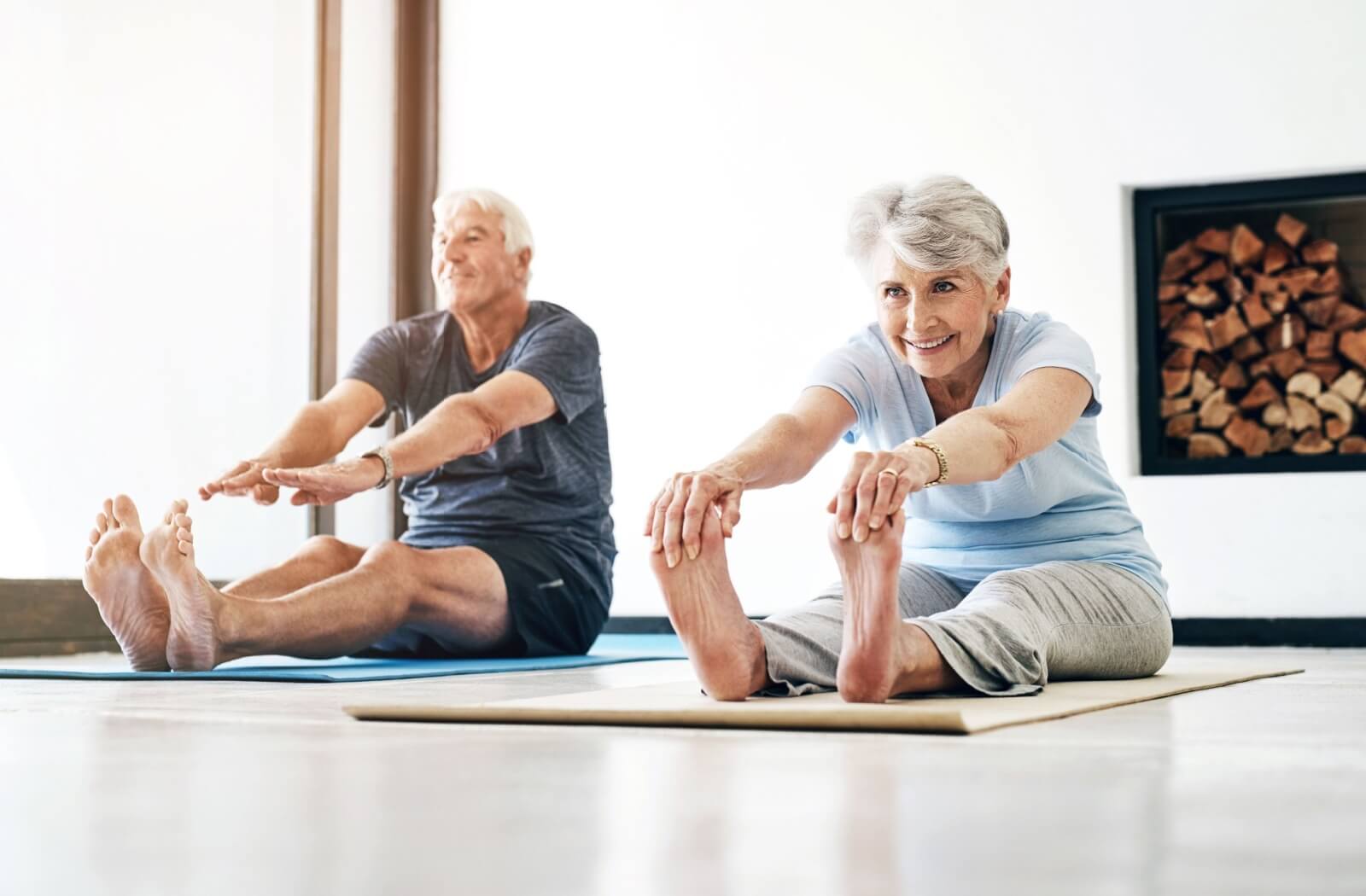 An older couple on yoga mats stretching forward during an exercise routine in senior living.