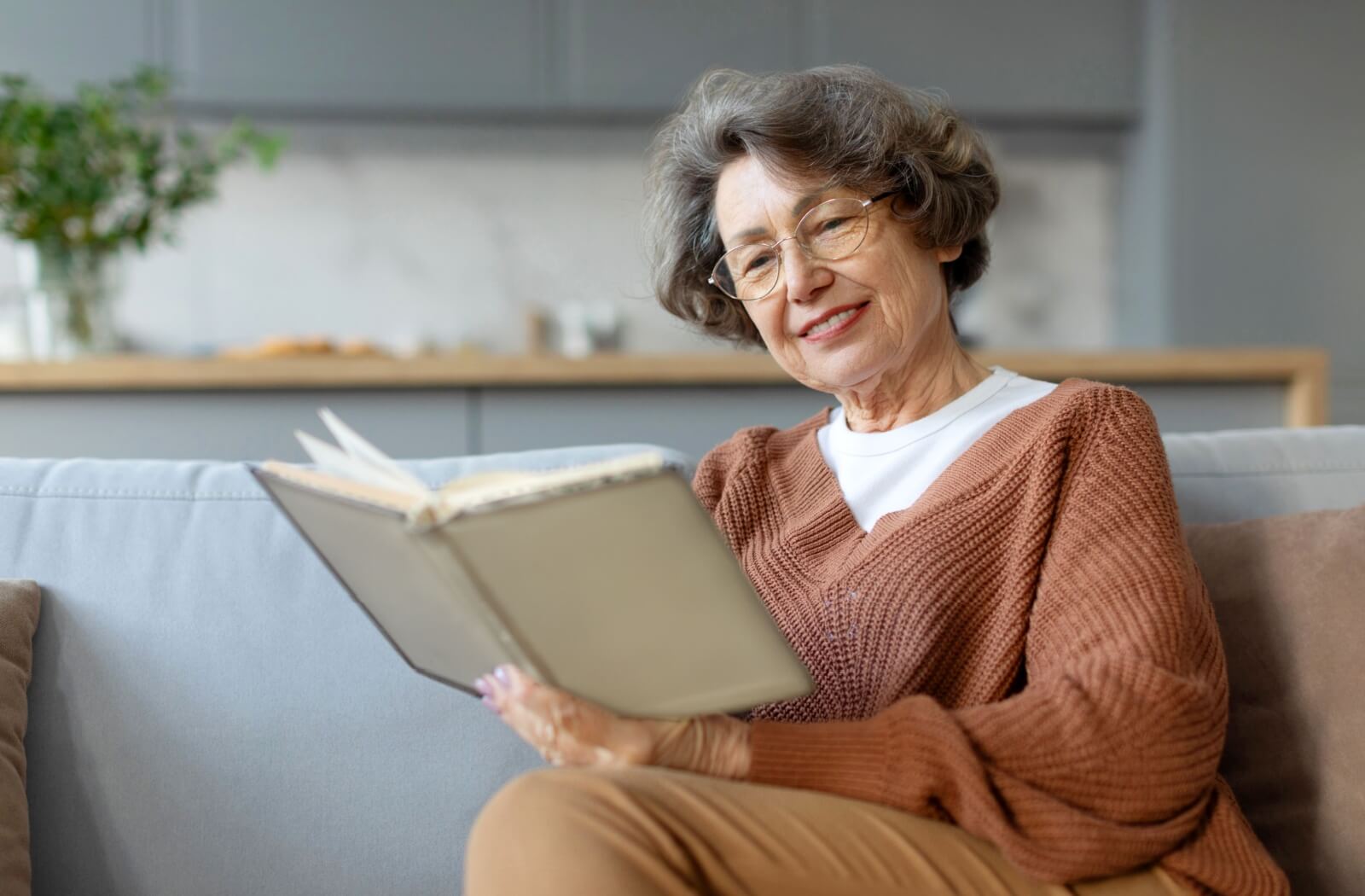 An older adult sitting on their couch, reading a book about Alzheimer's disease and smiling.