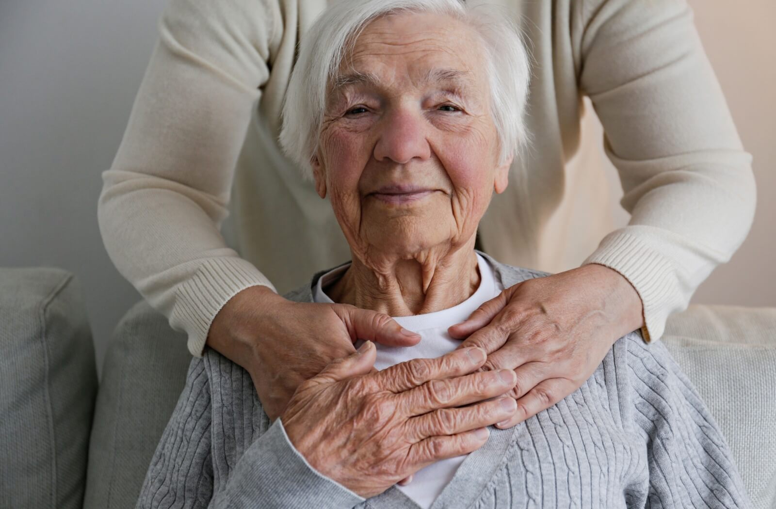 An out-of-frame caregiver hugging an older adult from behind in assisted living.