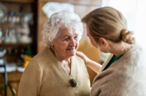An adult with their arm on the shoulder of an older adult with dementia, reassuring them during a conversation.