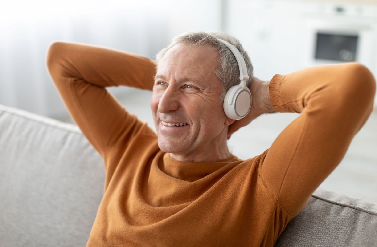 An older adult smiling with their arms behind their head, relaxing while listening to a podcast about history.