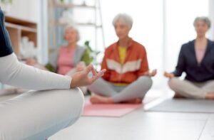 A group of 3 older adults in senior living meditating during a guided class to lower stress