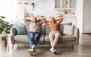 A senior couple relax on the couch in their new, clean, space after downsizing and decluttering their home.