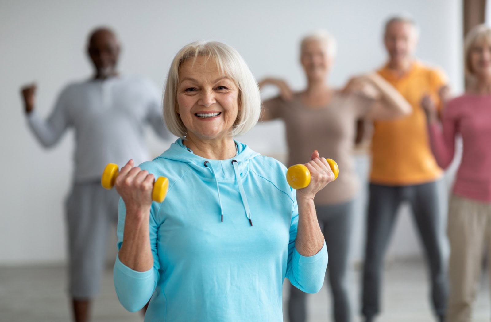 An older adult smiling while holding little yellow weights during their fitness class.