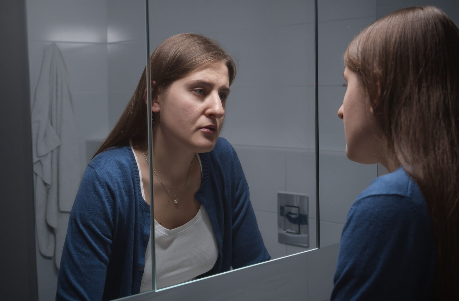 A caregiver stares in the mirror at the end of a long day. They look depressed and upset and like they don't recognize themselves.