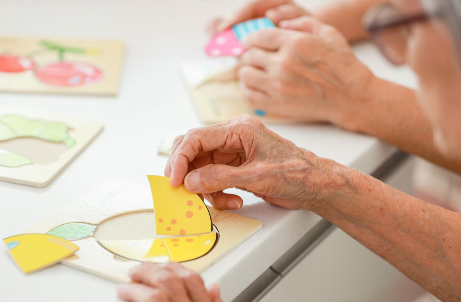 Close-up of seniors' hands doing a puzzle to help prevent dementia in a memory care community.