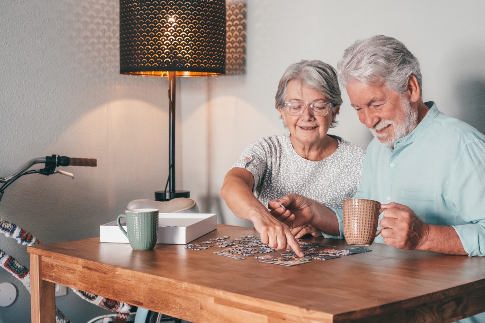 a senior couple sit at a table working on a pizzle in a memory care community