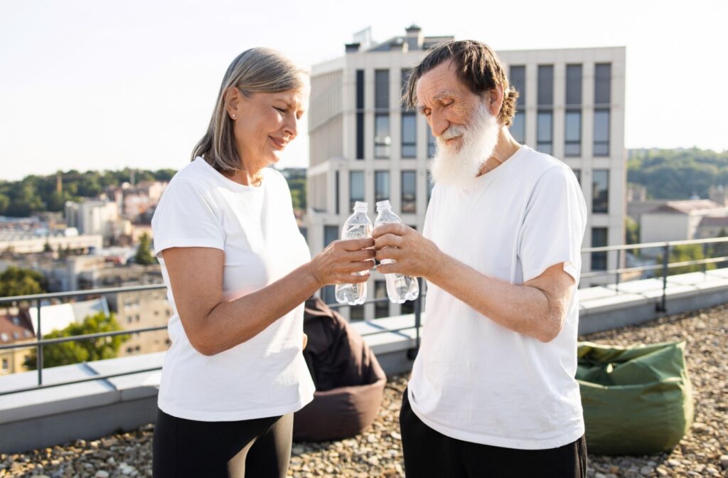 Two seniors in white t-shirts clink their water bottles together, holding each other accountable to drinking more water