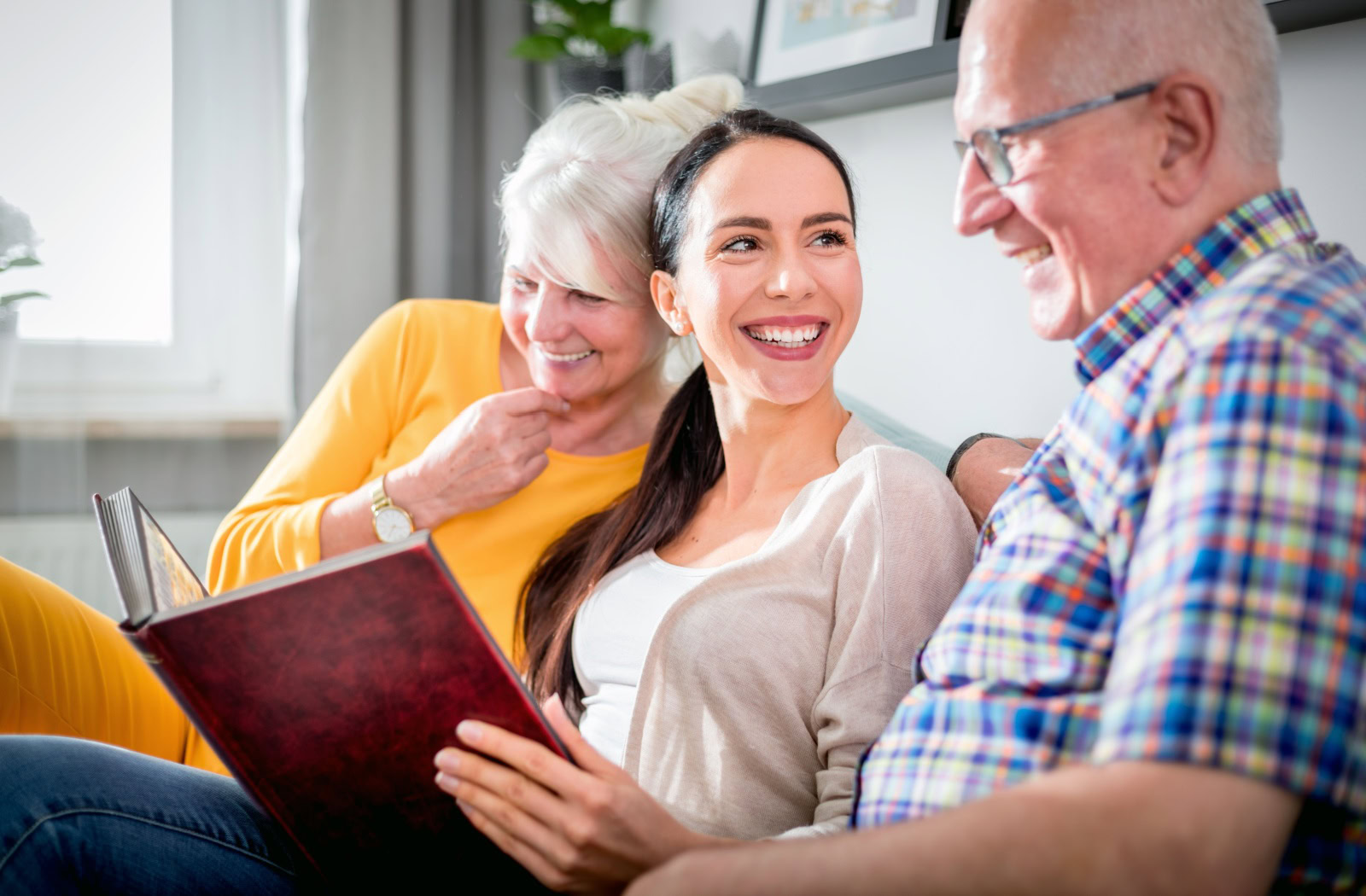Residents and a visiting loved one share smiles on the community couch, reminiscing over cherished memories in a photo album