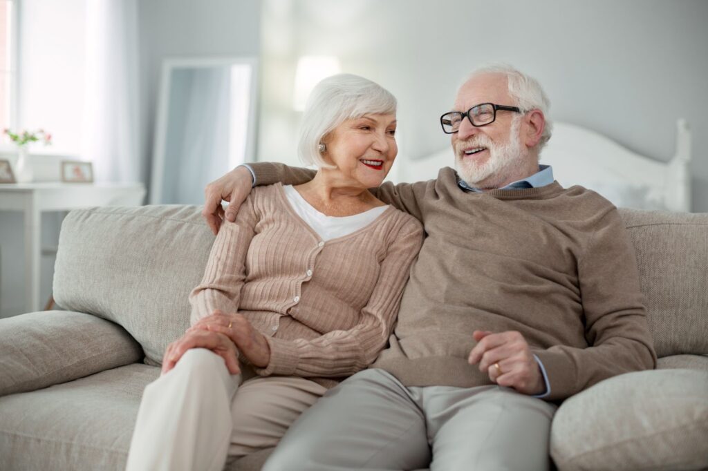 Happy senior couple relaxing on a couch, enjoying each other's company in a cheerful retirement community living room.