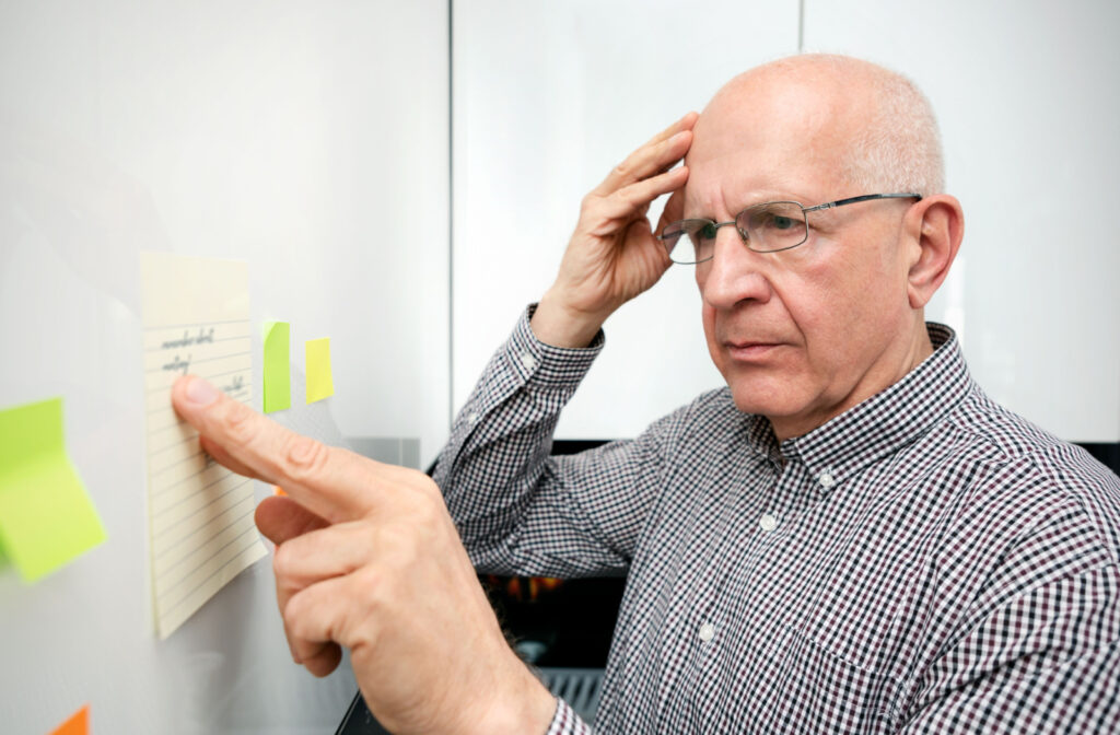 A senior with one hand placed on his head in confusion as they stand in front of a whiteboard reading sticky notes