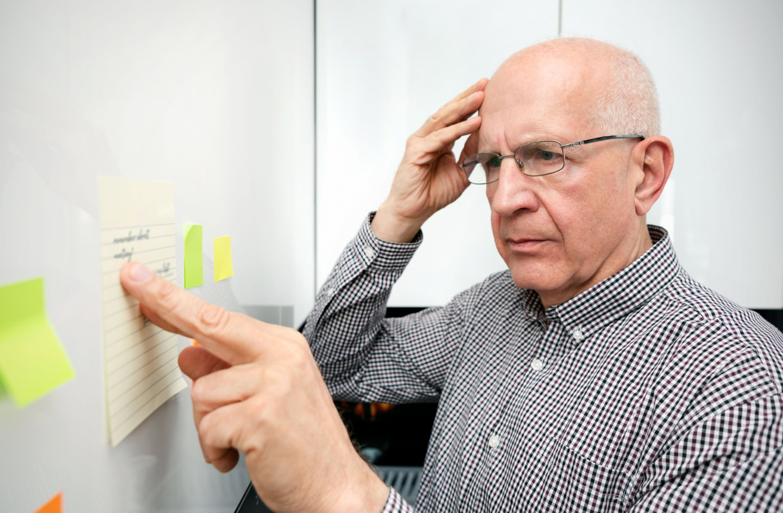 A senior with one hand placed on his head in confusion as they stand in front of a whiteboard reading sticky notes