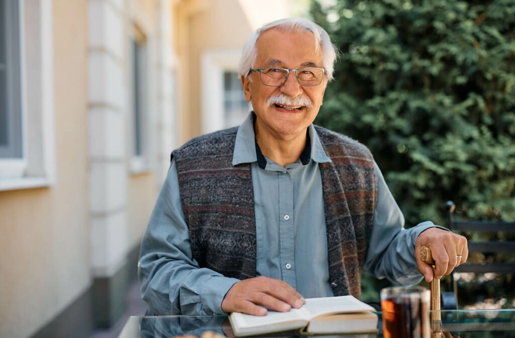 a senior sits smiling outside, reading a book